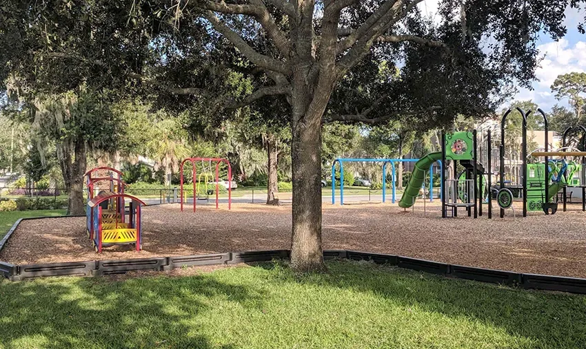 Área de recreação do Azalea Lane Playground em Winter Park, com  árvores, escorregadores e balanços para crianças