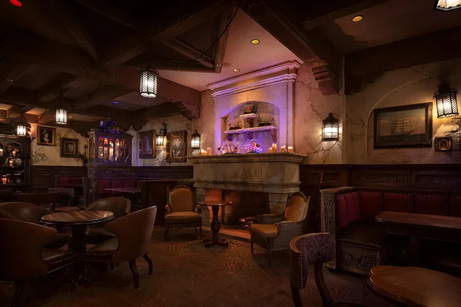Interior dos Aposentos dos Capitães no novo bar da Disney inspirado no Piratas do Caribe com lareira acesa, cortinas vermelhas e navios em miniatura dentro de garrafas.