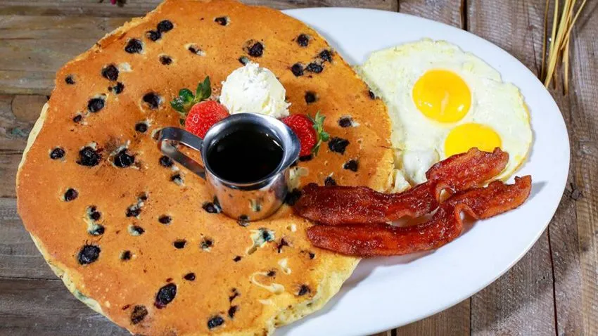 Prato de café da manhã da Hash House A Go Go, em Orlando, com porção generosa de panqueca, ovo frito e bacon
