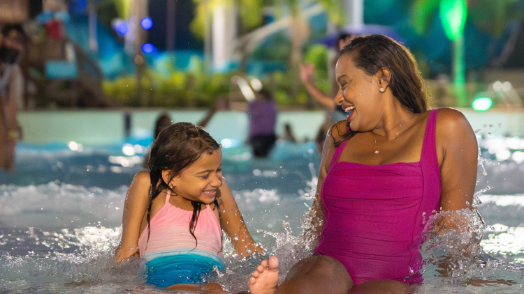Mulher e filha sentadas em uma piscina à noite