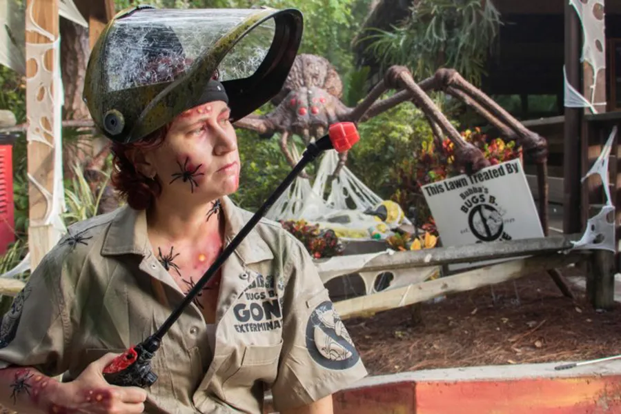 Pessoa com uniforme de caça-insetos e máscara repleta de aranhas procura por insetos gigantes no Gatorland
