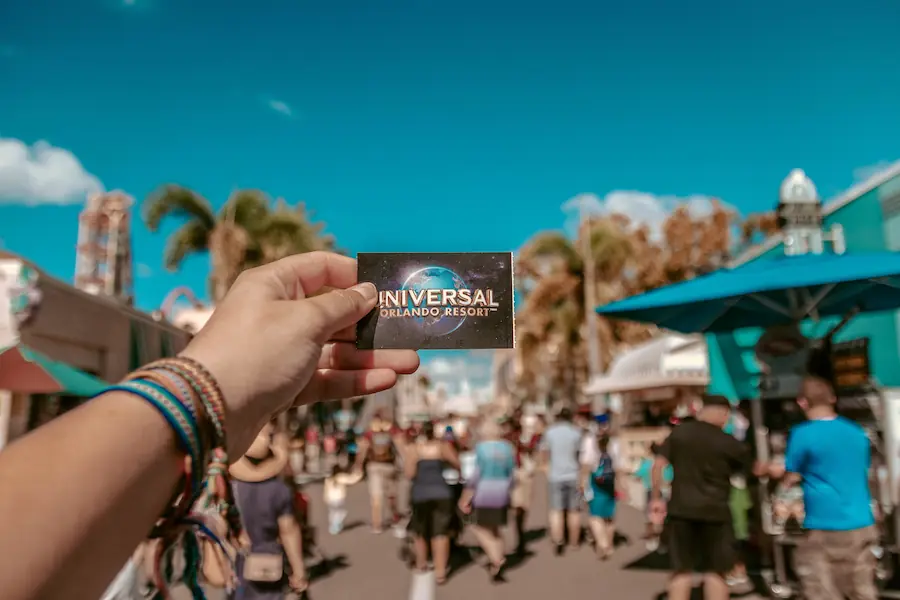 Pessoa estende ingresso da Universal Orlando Resorts com o parque ao fundo em um dia ensolarado